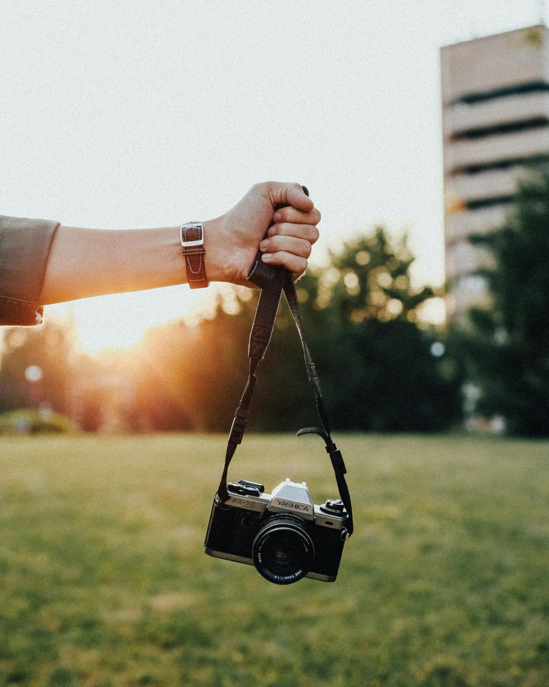 A hand lifts a Yashica film camera into grainy sunset light